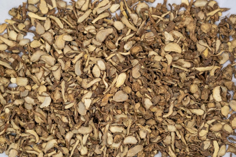 May include: A close-up of dried ginger root pieces. The pieces are chopped and vary in size and shape, with light tan and darker brown colours. The texture appears rough and fibrous, typical of dried ginger.