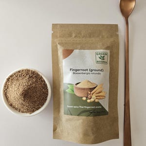 May include: A kraft paper bag of ground fingerroot with the text "Fingerroot (ground)" and "Boesenbergia rotunda". A small white bowl of ground fingerroot and a copper-coloured spoon are also present. The text reads "Sweet-spicy Thai fingerroot aroma."