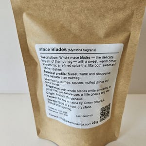 K&ouml;nnte beinhalten: Ein brauner Papierbeutel mit 25 g Muskatbl&uuml;ten (Myristica fragrans). Das wei&szlig;e Etikett enth&auml;lt eine detaillierte Produktbeschreibung, ein botanisches Profil, Anwendungshinweise, Herkunft, Lagerung, einen QR-Code und Kontaktinformationen.
