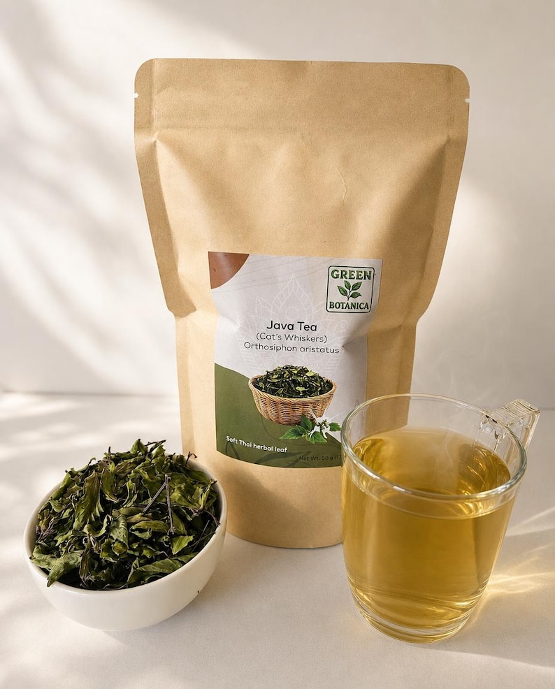 K&ouml;nnte beinhalten: Ein brauner Papierbeutel mit der Aufschrift Green Botanica Java Tea Cat's Whiskers Orthosiphon aristatus, eine wei&szlig;e Schale mit getrockneten gr&uuml;nen Kr&auml;uterbl&auml;ttern und eine klare Glastasse mit einem hellgoldenen Tee auf einer Fl&auml;che.