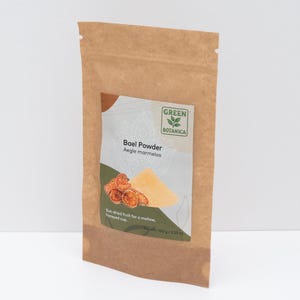 May include: A brown paper bag of Bael Powder from Green Botanica. The label shows a graphic of the powder and sun-dried fruit. The text on the label reads "Bael Powder Aegle marmelos" and "Sun-dried fruit for a mellow, honeyed cup." Net weight is 100g.