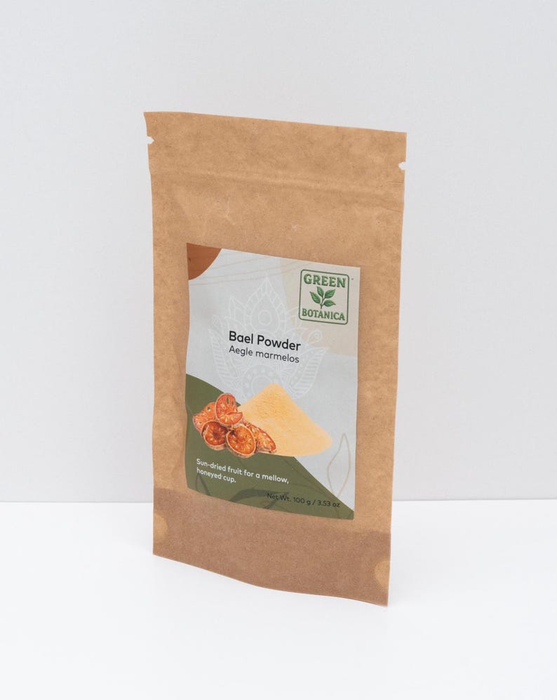 May include: A brown paper bag of Bael Powder from Green Botanica. The label shows a graphic of the powder and sun-dried fruit. The text on the label reads "Bael Powder Aegle marmelos" and "Sun-dried fruit for a mellow, honeyed cup." Net weight is 100g.