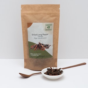 Peut inclure: Un sachet en papier brun &eacute;tiquet&eacute; Green Botanica Dried Long Pepper (whole) Piper retrofractum avec un poids net de 100 g / 3,53 oz. Un petit bol blanc rempli de poivres longs s&eacute;ch&eacute;s brun fonc&eacute; est devant avec une cuill&egrave;re en cuivre &agrave; long manche.