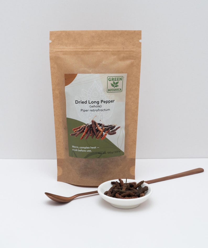 Peut inclure: Un sachet en papier brun &eacute;tiquet&eacute; Green Botanica Dried Long Pepper (whole) Piper retrofractum avec un poids net de 100 g / 3,53 oz. Un petit bol blanc rempli de poivres longs s&eacute;ch&eacute;s brun fonc&eacute; est devant avec une cuill&egrave;re en cuivre &agrave; long manche.