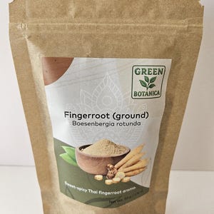 May include: A brown paper bag of ground fingerroot, labelled "Green Botanica." The label features an illustration of fingerroot and a bowl of powder. Text on the label reads "Fingerroot (ground) Boesenbergia rotunda" and "Sweet-spicy Thai fingerroot aroma." Net weight is 50g.