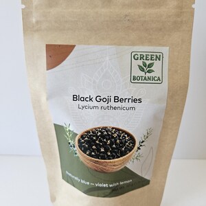 K&ouml;nnte beinhalten: Ein brauner Papierbeutel mit schwarzen Goji-Beeren, beschriftet als Lycium ruthenicum von Green Botanica. Das Etikett zeigt eine Holzschale mit dunklen Beeren, den Text Naturally blue - violet with lemon und ein Nettogewicht von 50g.