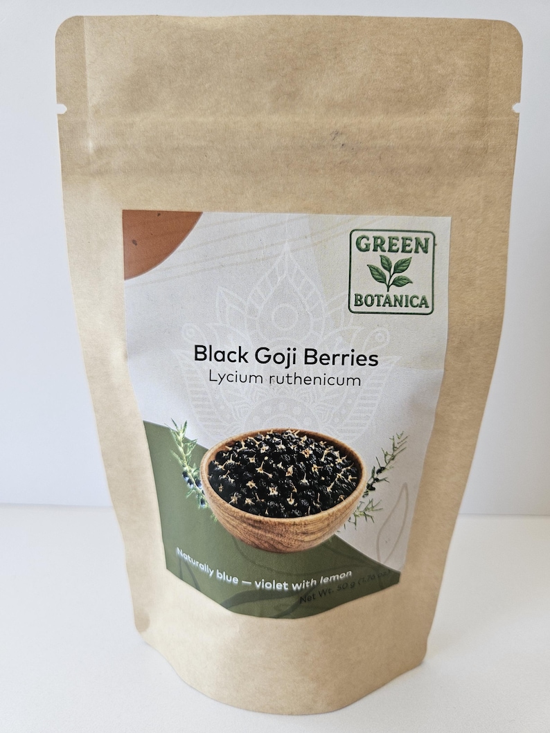 K&ouml;nnte beinhalten: Ein brauner Papierbeutel mit schwarzen Goji-Beeren, beschriftet als Lycium ruthenicum von Green Botanica. Das Etikett zeigt eine Holzschale mit dunklen Beeren, den Text Naturally blue - violet with lemon und ein Nettogewicht von 50g.