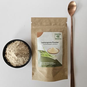 Pode incluir: Uma vista de cima mostra uma tigela preta com p&oacute; castanho claro, um saco de papel castanho com p&oacute; de capim-lim&atilde;o e uma colher longa de cobre. A embalagem diz "Lemongrass Powder" e "Green Botanica". O texto "Clean lemongrass aroma for curries, soups and blends" tamb&eacute;m &eacute; vis&iacute;vel.
