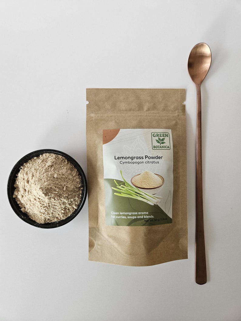 Pode incluir: Uma vista de cima mostra uma tigela preta com p&oacute; castanho claro, um saco de papel castanho com p&oacute; de capim-lim&atilde;o e uma colher longa de cobre. A embalagem diz "Lemongrass Powder" e "Green Botanica". O texto "Clean lemongrass aroma for curries, soups and blends" tamb&eacute;m &eacute; vis&iacute;vel.