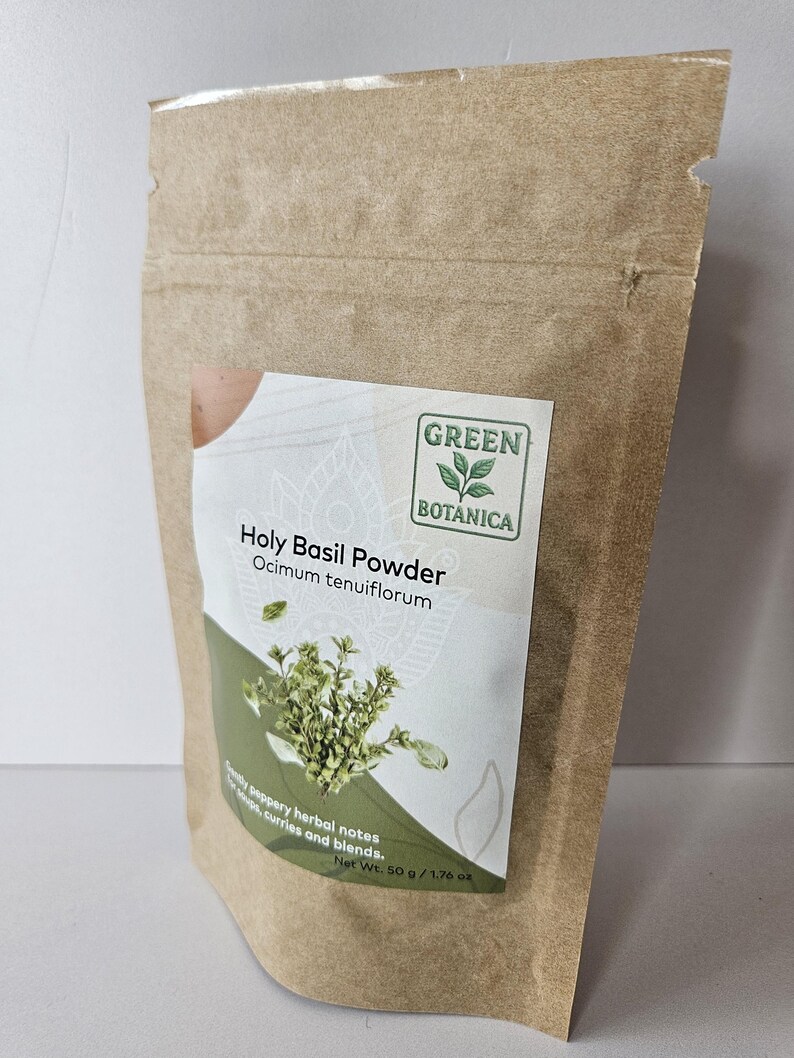 K&ouml;nnte beinhalten: Ein brauner Papiert&uuml;tchen mit Holy Basil Powder von Green Botanica. Das Etikett tr&auml;gt den Text "Holy Basil Powder" und "Ocimum tenuiflorum", mit einem Basilikumzweig und den Worten "pfeffrige Kr&auml;uternoten, Suppen, Currys und Mischungen." Das Nettogewicht betr&auml;gt 50 g.