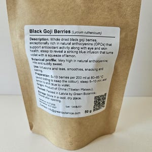 K&ouml;nnte beinhalten: Ein brauner Papierbeutel mit 50 g schwarzen Goji-Beeren (Lycium ruthenicum). Das wei&szlig;e Etikett enth&auml;lt eine Beschreibung, ein botanisches Profil, Anwendungshinweise, Zubereitungsdetails, Herkunft, Lagerungshinweise und einen QR-Code.