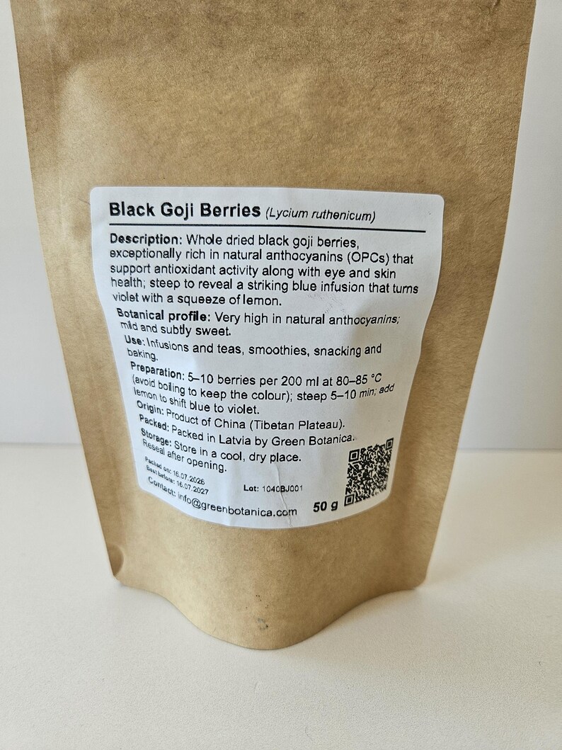 K&ouml;nnte beinhalten: Ein brauner Papierbeutel mit 50 g schwarzen Goji-Beeren (Lycium ruthenicum). Das wei&szlig;e Etikett enth&auml;lt eine Beschreibung, ein botanisches Profil, Anwendungshinweise, Zubereitungsdetails, Herkunft, Lagerungshinweise und einen QR-Code.