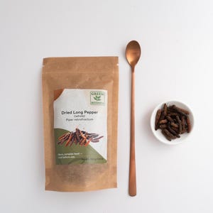 Peut inclure: Un sachet en papier brun &eacute;tiquet&eacute; Green Botanica Dried Long Pepper (whole) Piper retrofractum avec un poids net de 100 g / 3,53 oz, une longue cuill&egrave;re en m&eacute;tal cuivr&eacute; et un petit bol blanc rempli de morceaux de poivre long s&eacute;ch&eacute; brun fonc&eacute;.