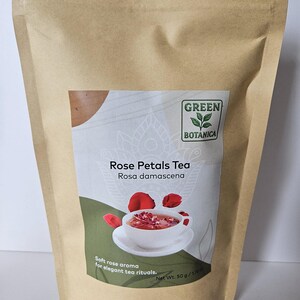 May include: A brown paper bag of Green Botanica Rose Petals Tea. The label shows a cup of tea with rose petals. Text on the label reads "Rose Petals Tea Rosa damascena" and "Soft rose aroma for elegant tea rituals."