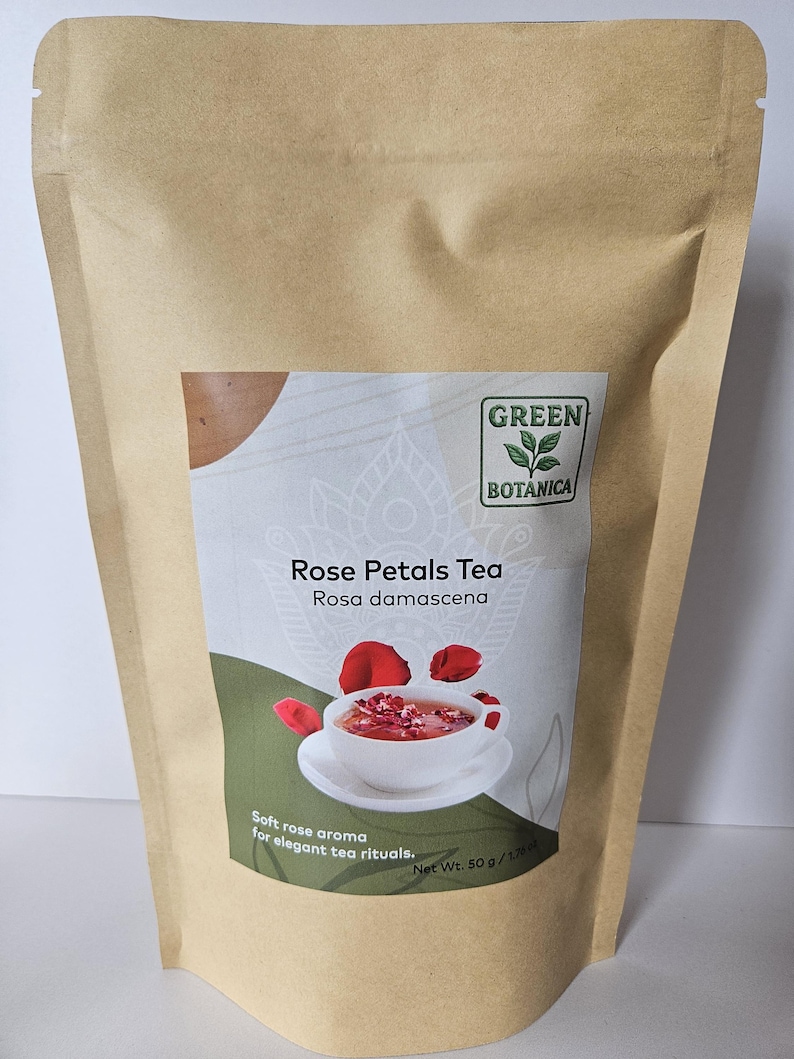 May include: A brown paper bag of Green Botanica Rose Petals Tea. The label shows a cup of tea with rose petals. Text on the label reads "Rose Petals Tea Rosa damascena" and "Soft rose aroma for elegant tea rituals."