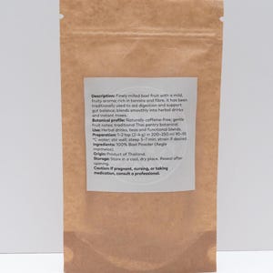 May include: A brown paper bag containing bael fruit powder. The label provides details about the product's aroma, uses, and preparation. The powder is a traditional Thai botanical, used in herbal drinks and teas. The bag is sealed.