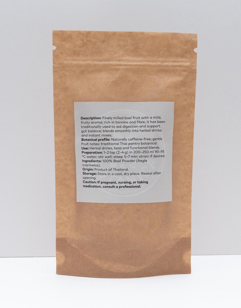 May include: A brown paper bag containing bael fruit powder. The label provides details about the product's aroma, uses, and preparation. The powder is a traditional Thai botanical, used in herbal drinks and teas. The bag is sealed.