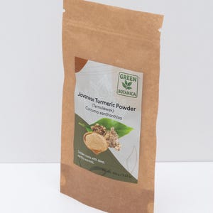 Op de afbeelding: Een bruine papieren zak met Javaans kurkumapoeder. Het etiket bevat de tekst "Javanese Turmeric Powder (Temulawak) Curcuma xanthorrhiza" met een illustratie van kurkumawortels en -bladeren. De zak bevat 100 g poeder.