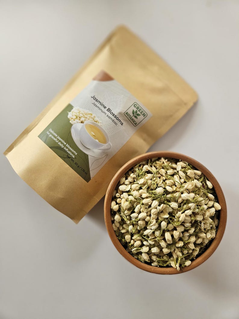 Peut inclure: Un bol en bois rempli de fleurs de jasmin s&eacute;ch&eacute;es &agrave; c&ocirc;t&eacute; d'un sac en papier kraft. Le sac porte une &eacute;tiquette indiquant "Jasmine Blossoms" et "Green Botanica". Les fleurs sont de couleur vert clair.