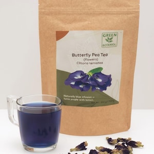 Pode incluir: Um saco de papel castanho com o r&oacute;tulo Green Botaniol Butterfly Pea Tea Clitoria ternatea com um peso l&iacute;quido de 200 g. Ao lado, uma caneca de vidro transparente cheia de l&iacute;quido azul escuro e v&aacute;rias flores secas roxas espalhadas.