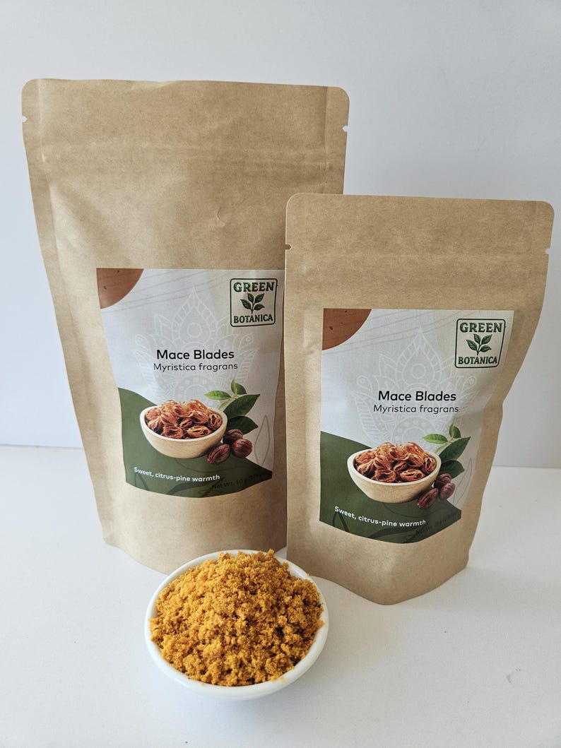K&ouml;nnte beinhalten: Zwei braune Papierbeutel mit der Aufschrift Green Botanica Mace Blades Myristica fragrans und einem Bild von Muskatbl&uuml;ten in einer Schale. Eine kleine wei&szlig;e Schale mit gemahlenem gelb-orangem Gew&uuml;rz steht vor den Beuteln auf einer wei&szlig;en Fl&auml;che.