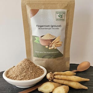 May include: A packet of ground fingerroot with the text "Fingerroot (ground) Boesenbergia rotunda" and "Sweet-spicy Thai fingerroot aroma." A small white bowl of ground fingerroot, fresh fingerroot, and a wooden spoon are also visible.