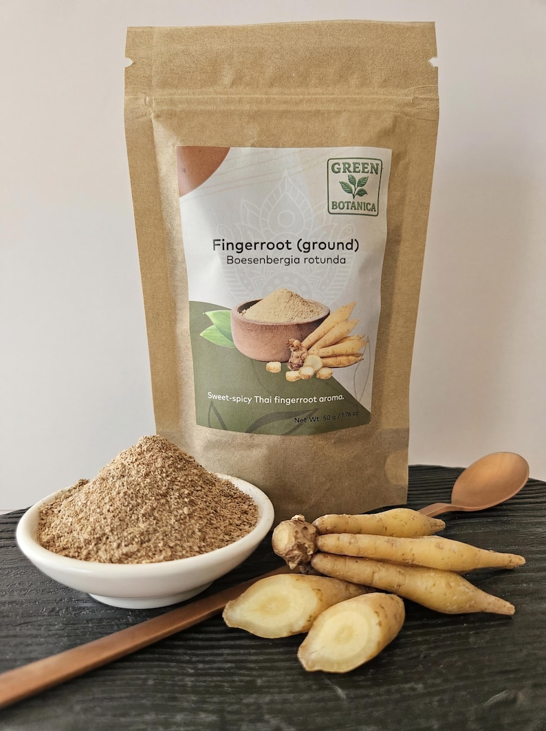 May include: A packet of ground fingerroot with the text "Fingerroot (ground) Boesenbergia rotunda" and "Sweet-spicy Thai fingerroot aroma." A small white bowl of ground fingerroot, fresh fingerroot, and a wooden spoon are also visible.