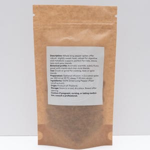 Peut inclure: Un sachet debout en papier kraft brun contenant des &eacute;pis de poivre long s&eacute;ch&eacute;s. Une &eacute;tiquette rectangulaire blanche sur le devant fournit des d&eacute;tails sur le produit, notamment la description, le profil botanique, la pr&eacute;paration et l'origine.