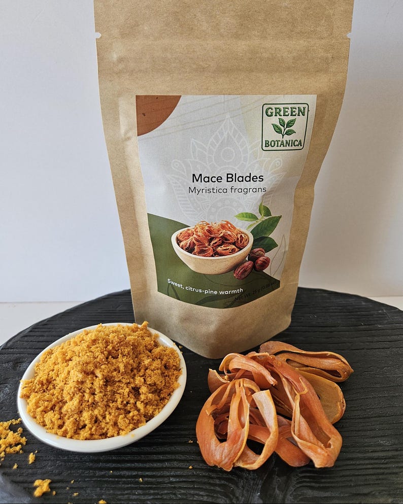K&ouml;nnte beinhalten: Ein brauner Papierbeutel mit der Aufschrift Green Botanica Mace Blades Myristica fragrans, eine wei&szlig;e Schale mit goldgelbem gemahlenem Muskatbl&uuml;tenpulver und ein kleiner Haufen getrockneter orangefarbener Muskatbl&uuml;ten. Das Etikett zeigt Muskatbl&uuml;ten.