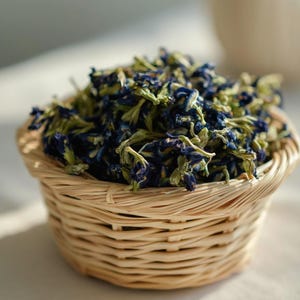 Pode incluir: Uma pequena cesta redonda de vime tran&ccedil;ado em tom castanho claro, cheia com um monte de flores de feij&atilde;o-borboleta secas. As flores s&atilde;o de um azul profundo com caules e c&aacute;lices verde-p&aacute;lidos, empilhadas densamente acima da borda.