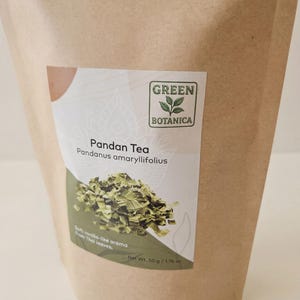 Może przedstawiać: Brązowa papierowa torba z etykietą z napisem "Pandan Tea" i "Green Botanica". Etykieta zawiera zielony wz&oacute;r liścia i stos suszonych liści zielonej herbaty. Tekst na etykiecie brzmi r&oacute;wnież "Miękki waniliowy aromat z tajskich liści."