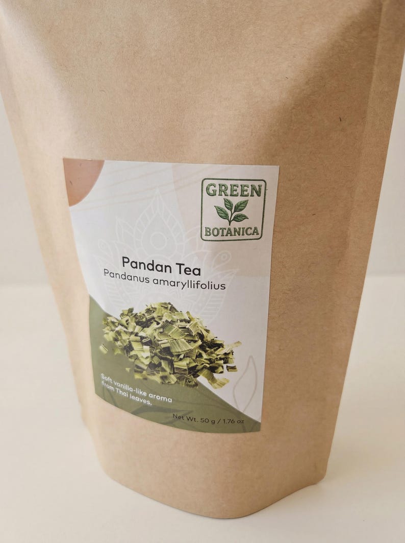 Może przedstawiać: Brązowa papierowa torba z etykietą z napisem "Pandan Tea" i "Green Botanica". Etykieta zawiera zielony wz&oacute;r liścia i stos suszonych liści zielonej herbaty. Tekst na etykiecie brzmi r&oacute;wnież "Miękki waniliowy aromat z tajskich liści."