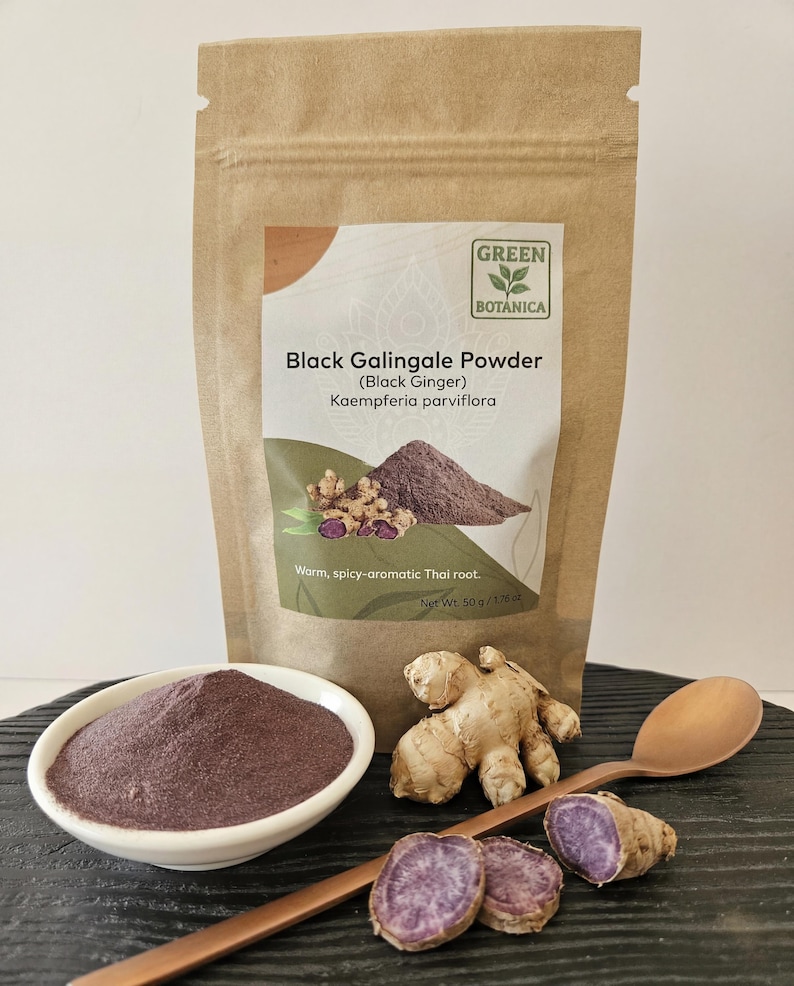 May include: A brown paper bag of Black Galingale Powder (Black Ginger) with the text "GREEN BOTANICA". A white bowl contains the powder, with a wooden spoon, ginger root, and sliced purple ginger root. The bag reads "Warm, spicy-aromatic Thai root."