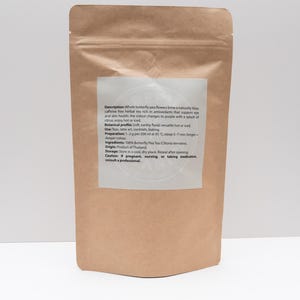 Pode incluir: Uma bolsa de papel castanho contendo flores de feij&atilde;o-borboleta. O r&oacute;tulo branco cont&eacute;m o texto: Description: Whole butterfly pea flowers brew a naturally blue, caffeine free herbal tea rich in antioxidants. Botanical profile: Soft, earthy floral; versatile hot or iced. Use: Teas, latte art, cocktails, baking. Preparation: 1-2 g per 200 ml at 95 &deg;C; steep 5-7 min. Ingredients: 100% Butterfly Pea Tea (Clitoria ternatea). Origin: Product of Thailand. Storage: Store in a cool, dry place. Caution: If pregnant, nursing, or taking medication, consult a professional.