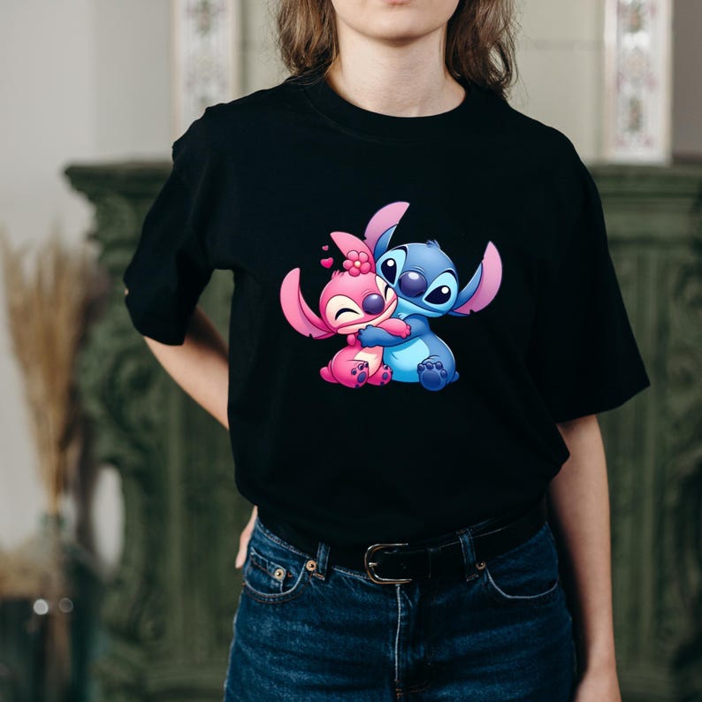 May include: Black t-shirt with a cartoon illustration of two characters, one pink and one blue, hugging. The pink character has a flower. The design is in the centre of the shirt.