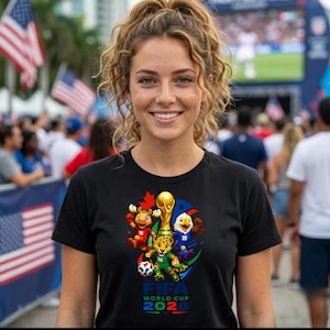 May include: A black short-sleeved t-shirt featuring a colorful graphic of the FIFA World Cup 2026 logo, including a golden trophy, a moose, a jaguar, and an eagle, with the text FIFA WORLD CUP 2026 printed in blue and green below the characters.
