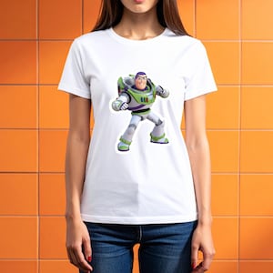 May include: White t-shirt featuring a colorful graphic of Buzz Lightyear from Toy Story. The character is depicted in his signature space ranger suit with green, white, and purple accents. The shirt is a classic crew neck style.