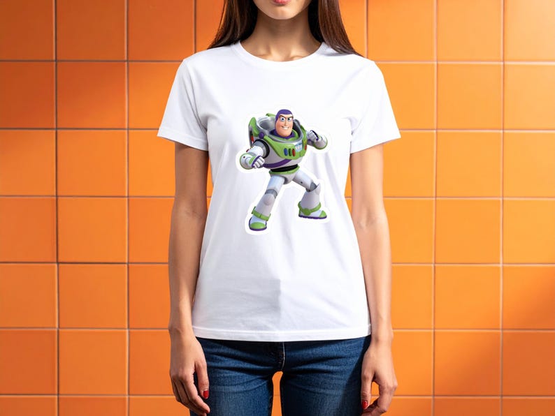 May include: White t-shirt featuring a colorful graphic of Buzz Lightyear from Toy Story. The character is depicted in his signature space ranger suit with green, white, and purple accents. The shirt is a classic crew neck style.