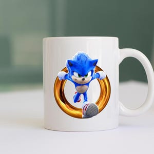 May include: White ceramic mug featuring a vibrant image of Sonic the Hedgehog in mid-run, framed by a golden ring. The blue character is depicted with his signature spiky hair and red and white shoes. A fun, colorful design for fans.