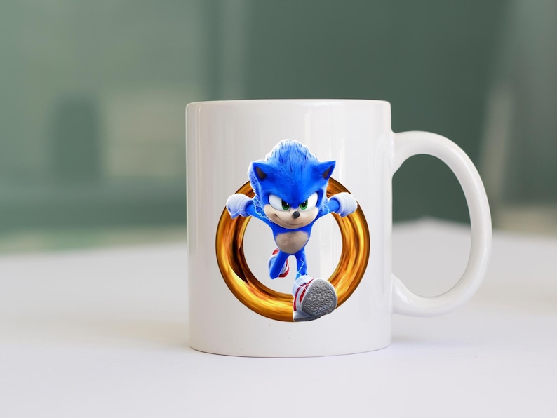 May include: White ceramic mug featuring a vibrant image of Sonic the Hedgehog in mid-run, framed by a golden ring. The blue character is depicted with his signature spiky hair and red and white shoes. A fun, colorful design for fans.