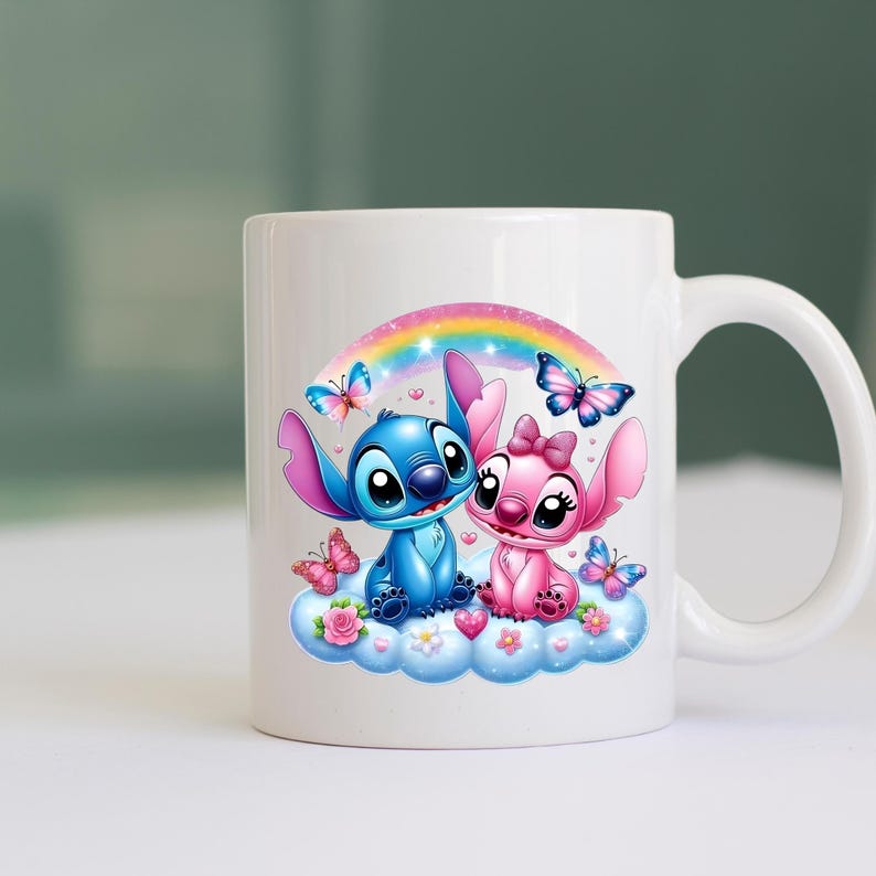 May include: White ceramic mug with a colourful illustration of two cartoon characters, one blue and one pink, on a cloud under a rainbow. Butterflies and flowers decorate the design.