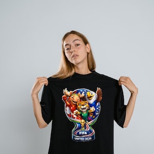 May include: A black t-shirt featuring a colorful graphic of the FIFA United 2026 logo, which includes a stylized trophy shape containing a moose, a jaguar, and an eagle, with the text FIFA UNITED 2026 printed clearly at the bottom of the design.