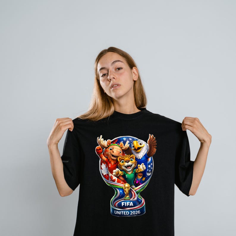 May include: A black t-shirt featuring a colorful graphic of the FIFA United 2026 logo, which includes a stylized trophy shape containing a moose, a jaguar, and an eagle, with the text FIFA UNITED 2026 printed clearly at the bottom of the design.