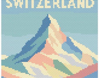 May include: A cross-stitch design featuring a mountain range with the word "SWITZERLAND" in light yellow at the top. The mountain is composed of blue, pink, yellow, and green hues against a light blue background.