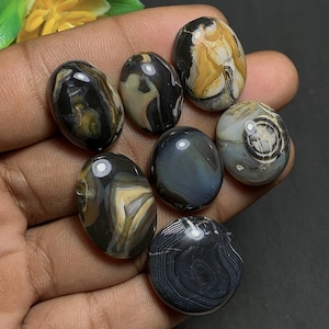 Peut inclure: Une collection de sept pierres précieuses polies de forme ovale. Les pierres présentent une variété de couleurs, dont le noir, le blanc, le beige et le gris, avec des motifs tourbillonnants uniques. Les pierres sont lisses et semblent naturelles, pour bijoux ou artisanat.