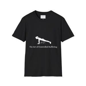 May include: A black short-sleeved t-shirt featuring a white graphic of a person in a plank position with wavy lines underneath. Below the graphic, the text reads, "The Art of Controlled Suffering" in a white serif font. The shirt has a crew neckline.