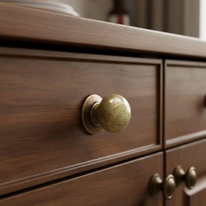 Peut inclure: Gros plan sur une commode en bois avec un tiroir. Le tiroir est orné d'un bouton rond en forme de bille, avec un aspect marbré et une base en laiton. Le bois est brun foncé.
