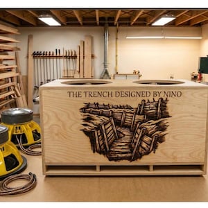 Può includere: Un box per altoparlanti in legno con la scritta "THE TRENCH DESIGNED BY NINO" e un'immagine di trincea pirografata. Due grandi altoparlanti gialli con la parte superiore argentata sono davanti. Gli altoparlanti hanno un diametro di circa 46 cm.