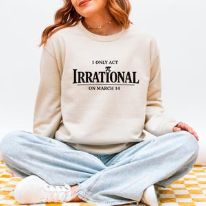 May include: Beige sweatshirt with the text "I only act irrational on March 14". The word "Irrational" is in a bold, black, serif font. The wearer is sitting cross-legged on a yellow and white checkered surface.