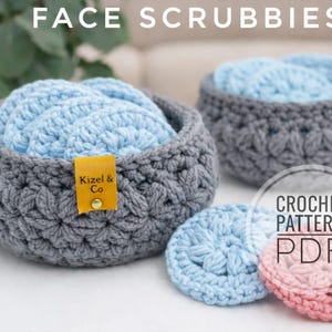 May include: Two gray crocheted baskets filled with light blue face scrubbies. Two additional scrubbies, one light blue and one pink, are next to the baskets. The text "FACE SCRUBBIES" is at the top of the image. A yellow tag with "Kizel & Co" is attached to one basket.
